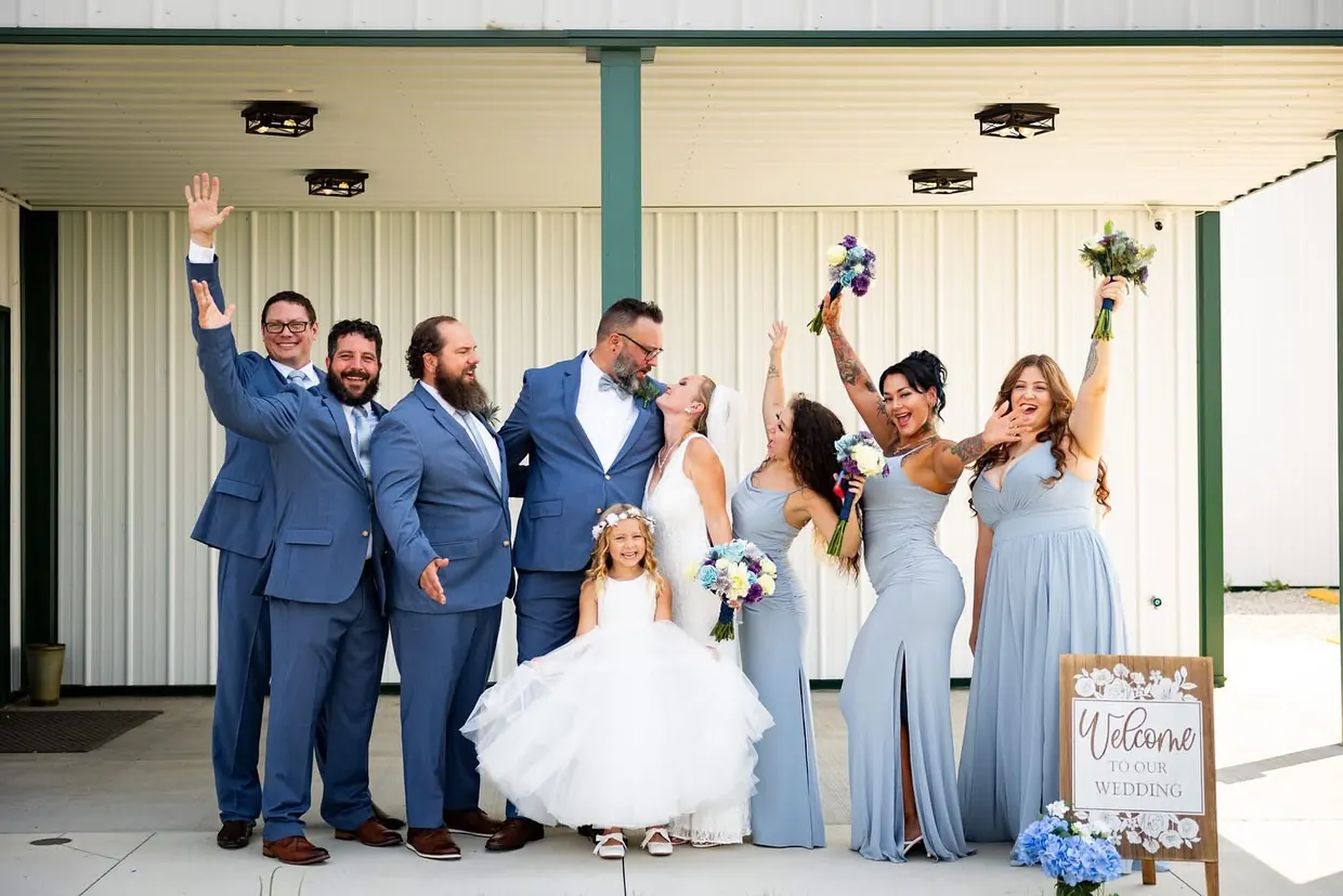 Bride, groom and wedding party in blue celebrating on the covered patio at Barn at the Lucky Farm